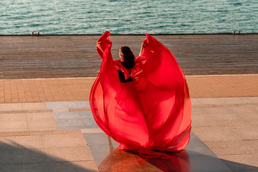 Sunrise red dress. A woman in a long red dress against the backdrop of sunrise, bright golden light of the sun's rays. The concept of femininity, harmony