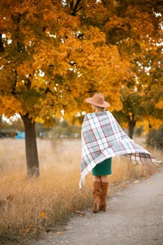 autumn woman in a green dress, brown hat, plaid, against the background of an autumn tree.