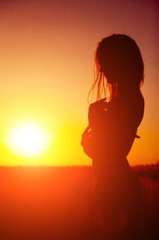 Silhouette of a young woman at sunset in the field. Beautiful slender girl in underwear posing outdoors in the rays of the sun