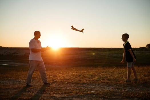 Soft focus of father and son playing toy airplane in meadow at sunset with happy emotions. Family, vacation and travel concept. At sunset in summer they launch an airplane against background sky