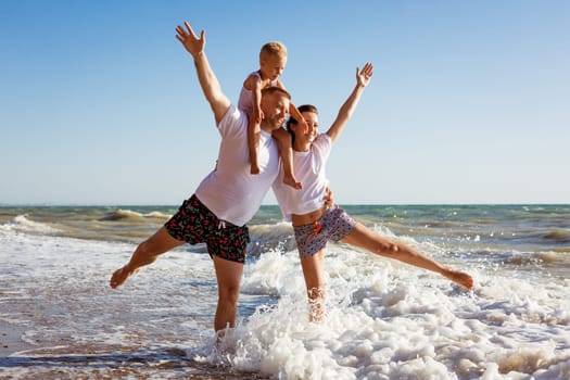 Happy family having fun on summer vacation. Happy son sits on his dad's neck. Cheerful young family on the seashore. Summer holidays for the whole family