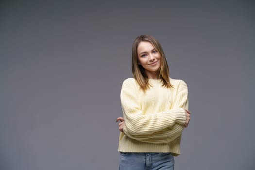 Portrait of a cute young woman of Caucasian ethnicity in a yellow sweater on a gray background looking at the camera. Beautiful confident girl