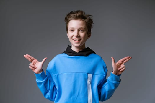 Portrait of a cute guy of European appearance with a snow-white toothy smile in a blue sweatshirt posing on a gray background