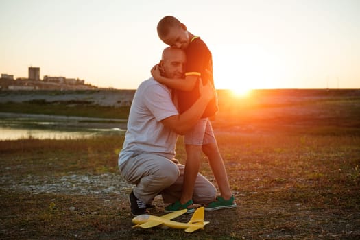 Father's day. Dad and little son play together outdoors toy airplane in the meadow at sunset with happy emotions. Family, vacation and travel concept.