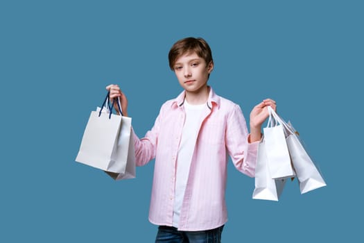 a young handsome guy of European appearance in a pink bag and a white fetball , cap holds paper bags in his hands with purchases on a blue background