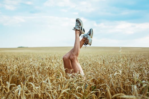 Sexy woman legs on blue sky and wheat field background. Summer vacation concept . Relaxing on a sunny day in the field