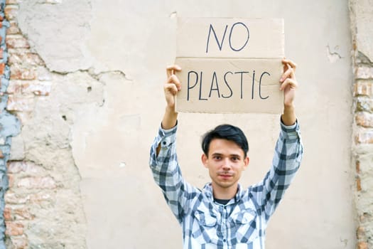 Young man with the inscription on the cardboard no plastic. Caucasian guy at a demonstration against environmental pollution, to help protect the environment. For a clean eco system on the planet