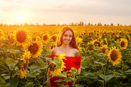 Young woman smiling at sunset in a field of sunflowers. A cute girl of Caucasian appearance in a red dress is happy and free to stand in the evening in the rays. Natural beauty in nature