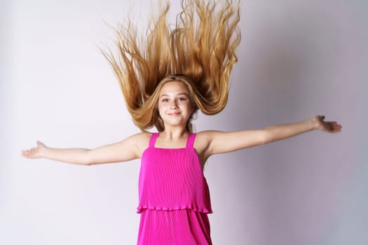 A cute and happy girl of Caucasian appearance in pink clothes on a white background plays with her long hair.