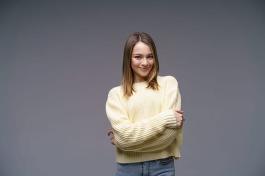 Portrait of a cute young woman of Caucasian ethnicity in a yellow sweater on a gray background looking at the camera. Beautiful confident girl