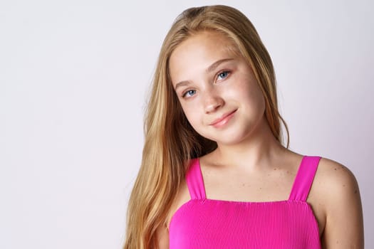 Portrait of a cute girl of blonde Caucasian ethnicity posing on a white background in pink clothes close-up. Happy teenager
