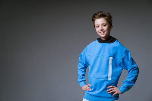 Portrait of a cute guy of European appearance with a snow-white toothy smile in a blue sweatshirt posing on a gray background