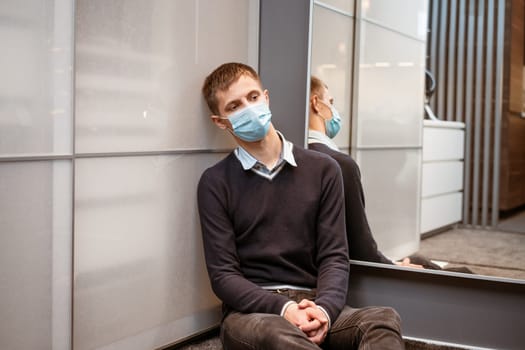 a guy of Caucasian nationality sits in a corner wearing a protective mask sad at the mirror.