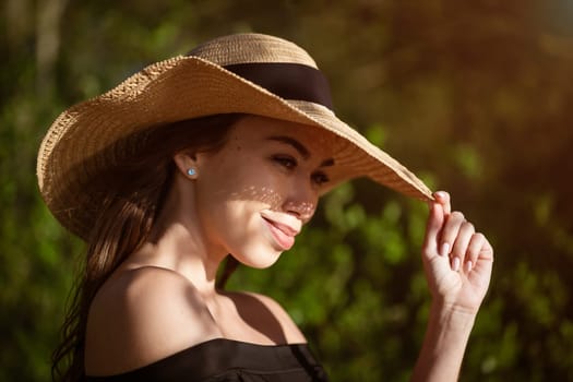 Beautiful young woman in a straw hat in black outdoors on a sunny day smiling, close-up. Happy caucasian girl in the summer on nature