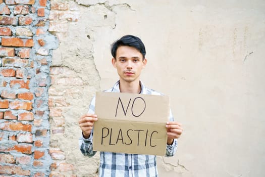 Caucasian guy holding the inscription no plastic. Environmental protection concept from garbage pollution . Young man protesting with placard banning plastic against cement wall background