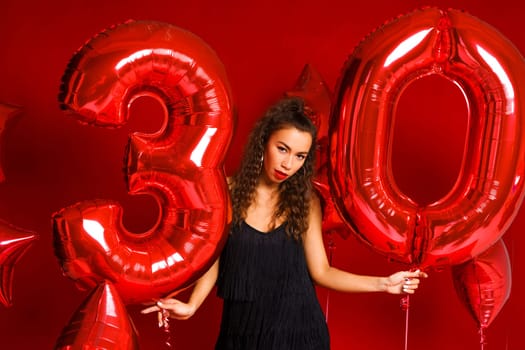 Valentine Beauty girl with red balloon. Beautiful Happy Caucasian Young woman Holiday party, birthday. Joyful model - Image. On a red background, red balloons in the form of numbers 30