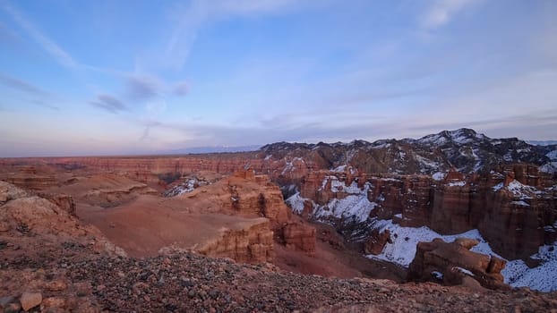 Grand Canyon Charyn. Orange cliffs and rocks. In places there are dry bushes and there is snow. The sun is shining brightly. White clouds. Beautiful sunset and sunrise. The place looks like Mars