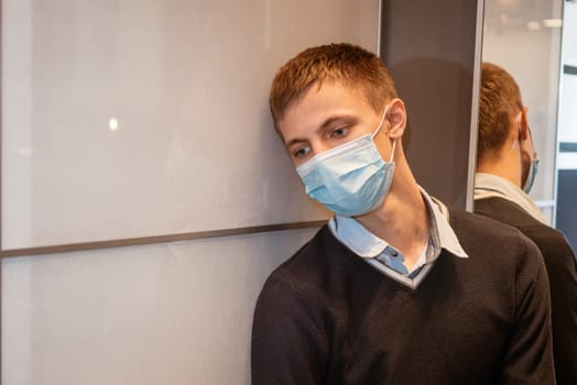 a guy of Caucasian nationality sits in a corner wearing a protective mask sad at the mirror.