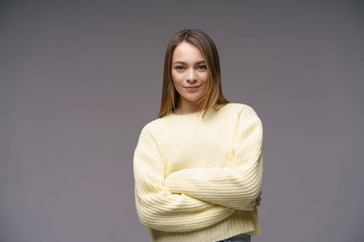 Portrait of a cute young woman of Caucasian ethnicity in a yellow sweater on a gray background looking at the camera. Beautiful confident girl