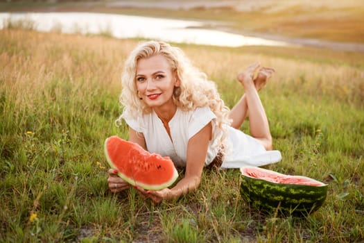 Portrait of a cute woman with a piece of watermelon in her hand in nature. Cheerful girl eating ripe red watermelon. Summer mood in nature with watermelon