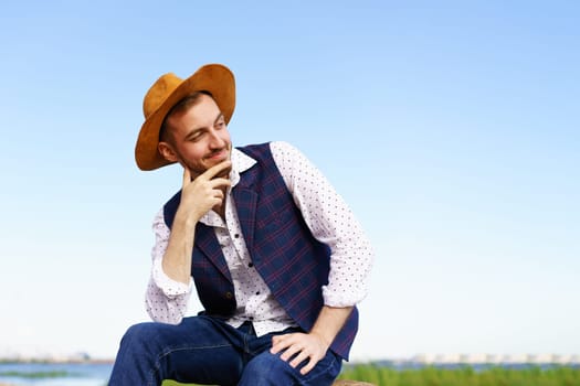 Close up portrait of handsome stylish casual man traveler in hat sitting at sea coastline and enjoying peaceful nature. Close-Up Of Man Wearing Hat Against Sky.