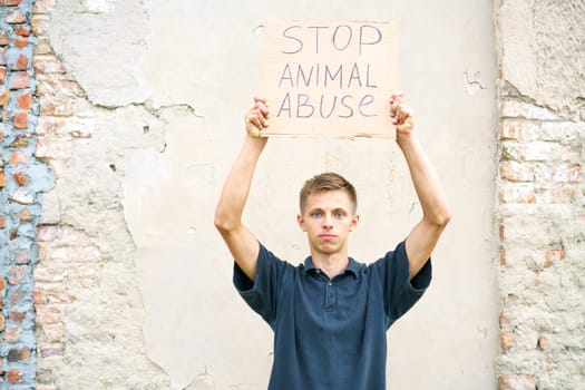 Young man holding the inscription stop animal abuse in his hands. Caucasian guy in protection of animals came out to protest. Animal rights conceptual image