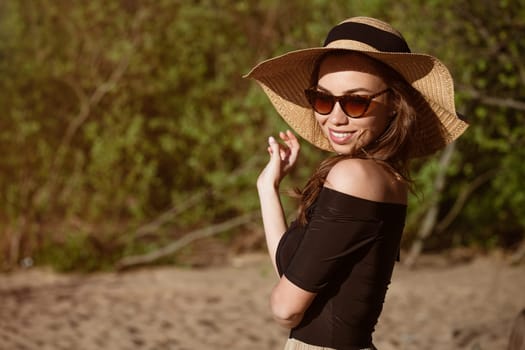 Beautiful young woman in a straw hat in black outdoors on a sunny day smiling, close-up. Happy caucasian girl in the summer on nature