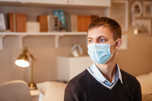 a young guy of European appearance, sitting comfortably on the couch in a medical mask. Concept to wait out the pandemic while sitting at home