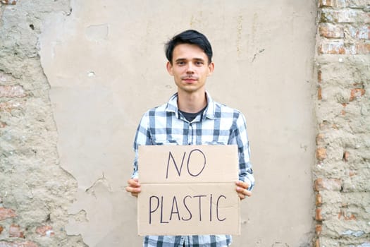 Young man with the inscription on the cardboard no plastic. Caucasian guy at a demonstration against environmental pollution, to help protect the environment. For a clean eco system on the planet