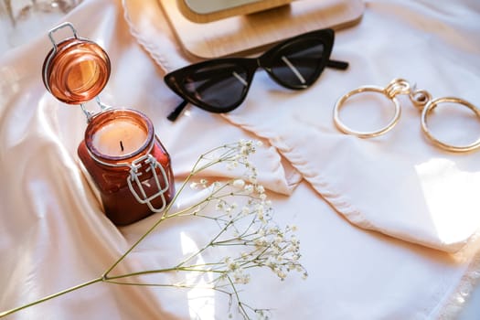 there is a decorative candle in a jar on the fabric, black glasses and jewelry with a mirror, soft focus