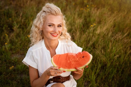 Portrait of a cute woman with a piece of watermelon in her hand in nature. Cheerful girl eating ripe red watermelon. Summer mood in nature with watermelon