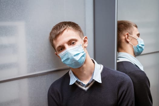 a guy of Caucasian nationality sits in a corner wearing a protective mask sad at the mirror.