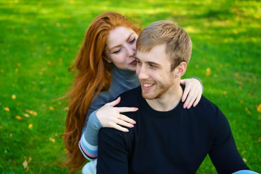 Cheerful young couple guy and red-haired girl of Caucasian ethnicity , are having fun together in the park on green grass on a sunny summer day in casual clothes