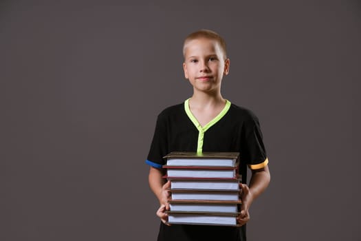 schoolboy boy in black t-shirt holding a stack of books on a gray background