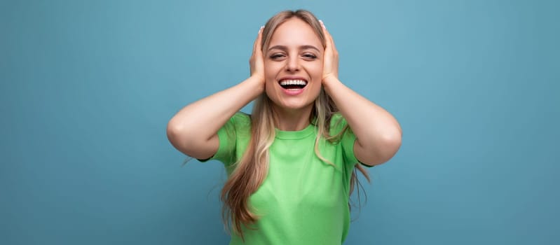 young smiling woman in casual attire covered her ears from a loud sound on a blue isolated background.