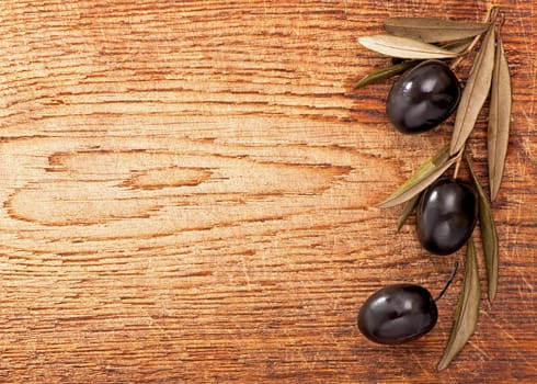 Olives over Wooden Background. Dark olives with leaves on wooden background, old wooden table, olive branch, background.