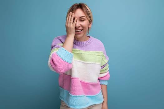 charming blond young woman covered her face with her hand and smiles on a blue background.