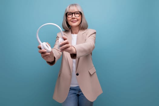 mature 60s business woman listening to music in big headphones on a bright background with copy space.