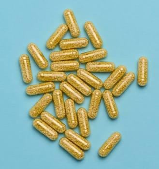 Transparent medical capsules with yellow granules inside on a blue background, tablets for treatment, vitamins