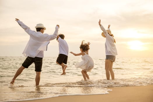 Happy Asian family have fun jumping together on beach in holiday at sunset time, Silhouette of family holding hands live healthy lifestyle on beach, back people enjoying travel and vacations concept