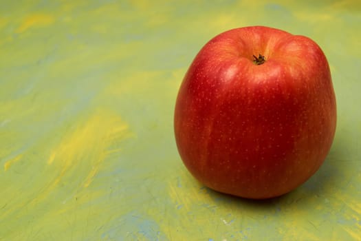 Single red apple on yellow background with copy space