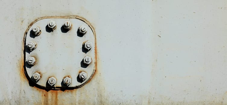 Large nuts and bolts on gray steel plate of rail bridge, lit by bright sun. Abstract industrial background, space for text on the right.