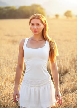 Young woman in white dress, sun back light wheat field in background.