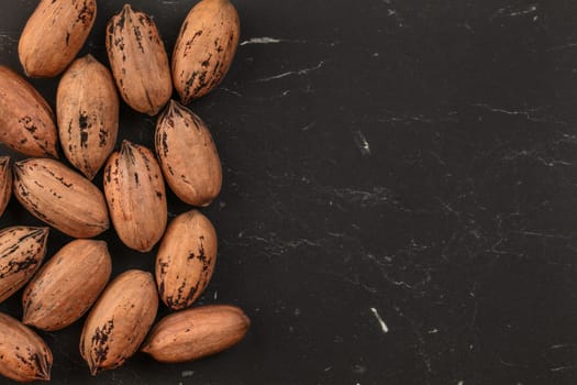 Tabletop view, whole pecan (Carya illinoinensis) nuts with spots on shells (Turkish variety) on black marble desk, space for text on right side.