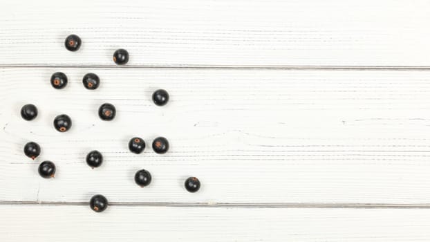Tabletop view blackcurrants scattered on white boards, space for text on right side.