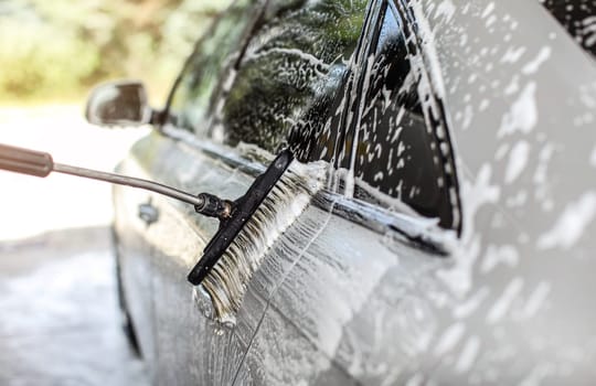 Side of silver car washed in self service manual carwash. Brush leaving strokes in white shampoo foam.