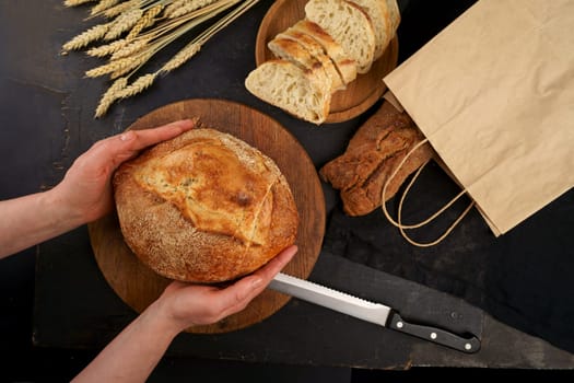 Whole grain bread put on kitchen wood plate with knife for cut. Fresh bread on table close-up. Fresh bread on the kitchen table. The healthy eating and traditional bakery concept. Top viev.