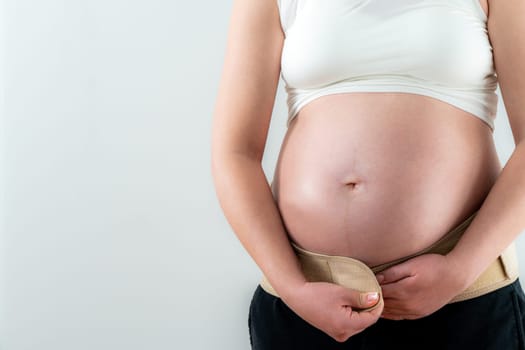 Pregnant woman putting on supporting bandage to reduce backache