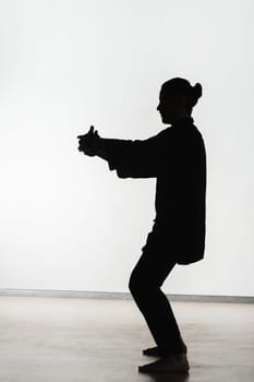 Silhouette of a person practicing qigong energy exercises on a light background.