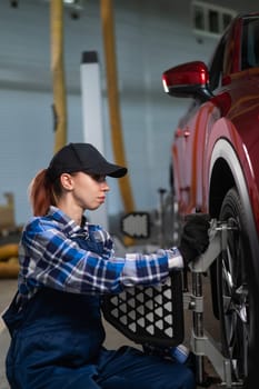 A female auto mechanic makes a camber. Woman working in a car service